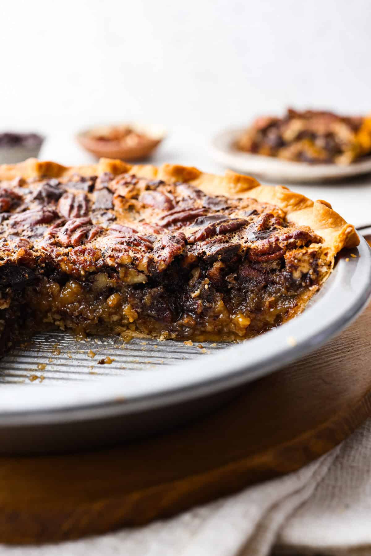 Side shot of chocolate pecan pie in a pie pan with a slice taken out showing the gooey inside. 