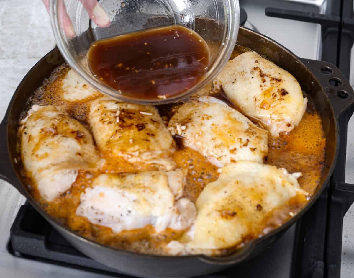 Angle shot of someone pouring sauce over chicken thighs in skillet. 