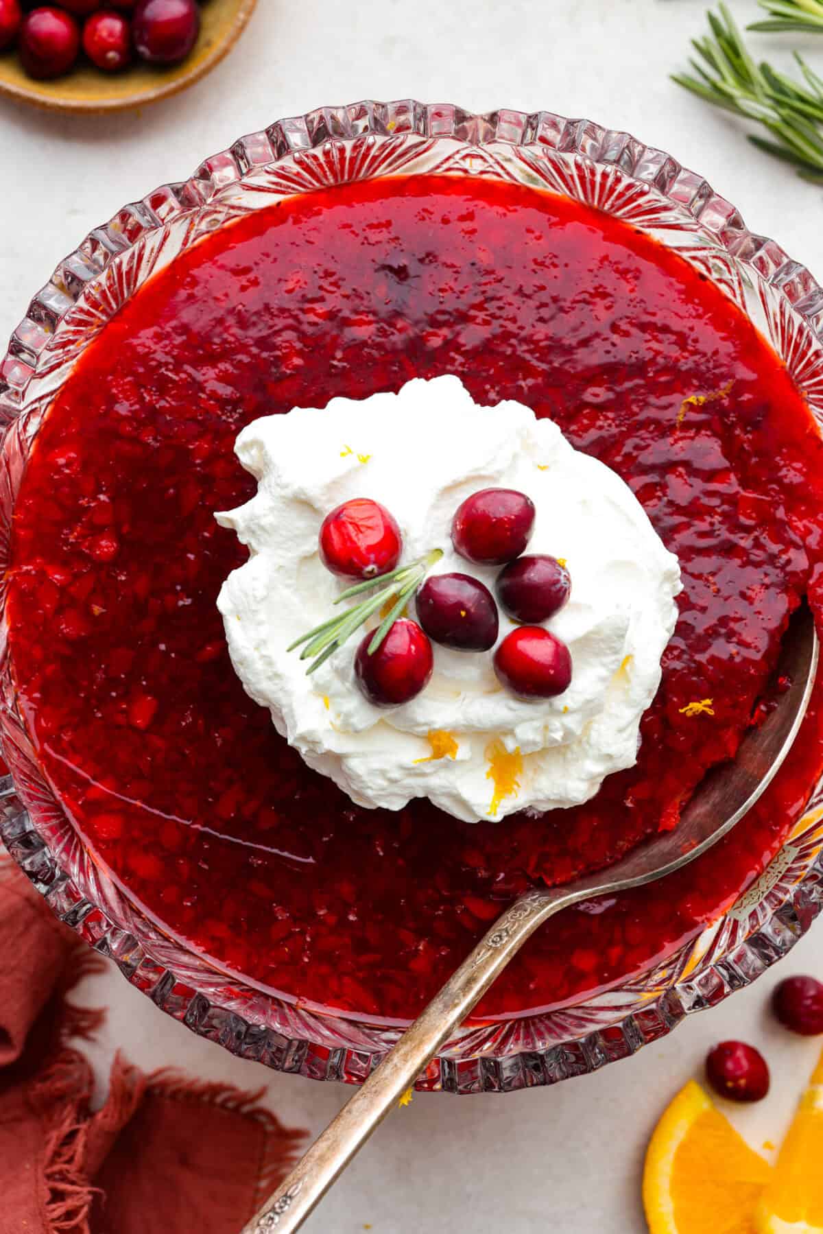 Overhead shot of cranberry jello salad with whipped cream on top and whole cranberry garnish. 