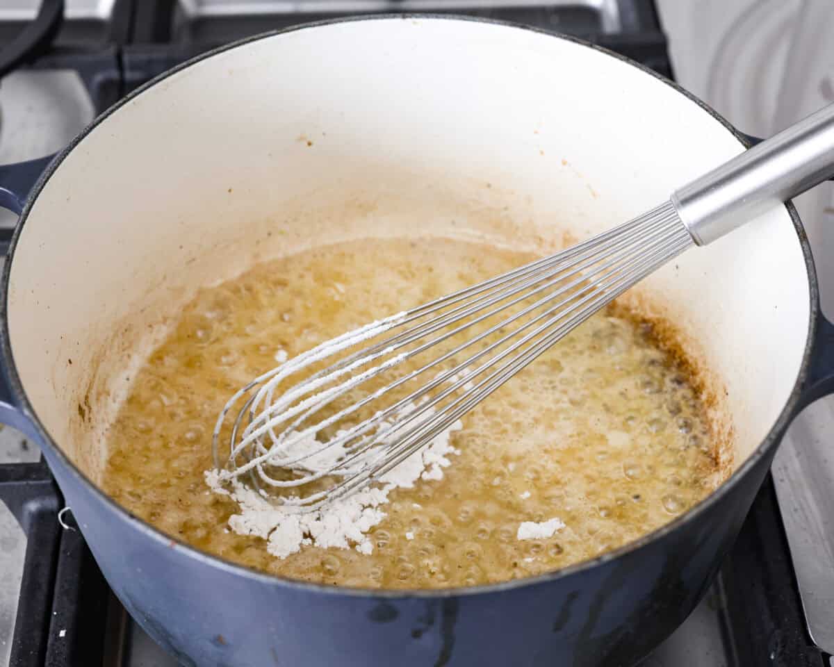 Angle shot of someone whisking four into the melted butter in the pot. 