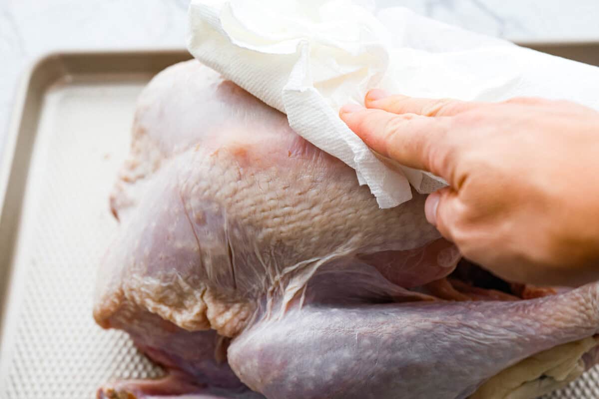 Angle shot of someone patting the turkey dry with a paper towel.