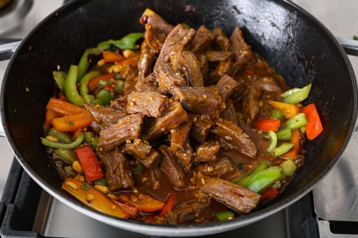 Close up shot of cooked kung pao beef being added back to the wok with the veggies. 