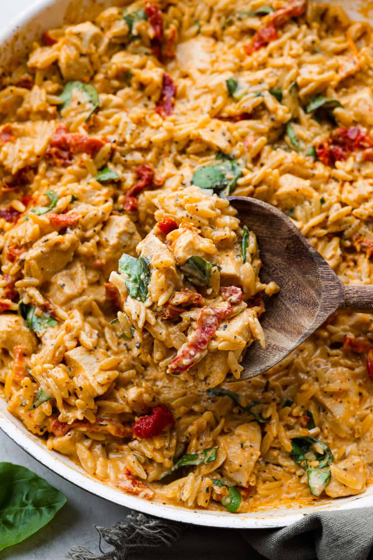 Close up shot of a scoop of marry me chicken orzo being taken out of the pan.