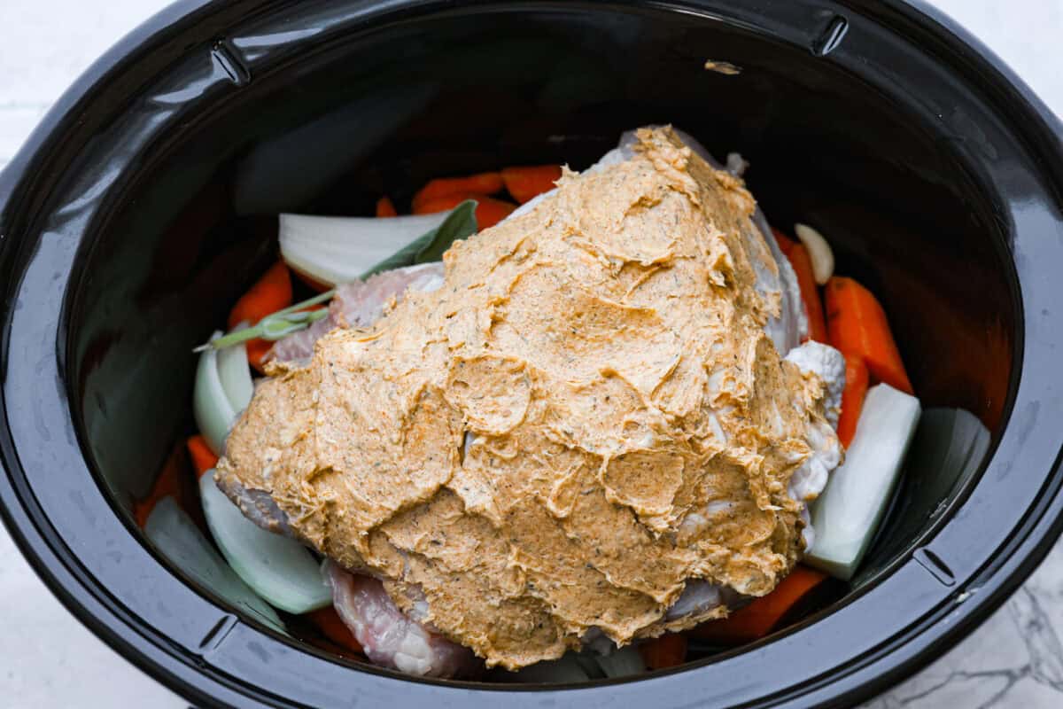 Overhead shot of the turkey breast covered in herbed butter on top of the vegetables in the crock pot. 