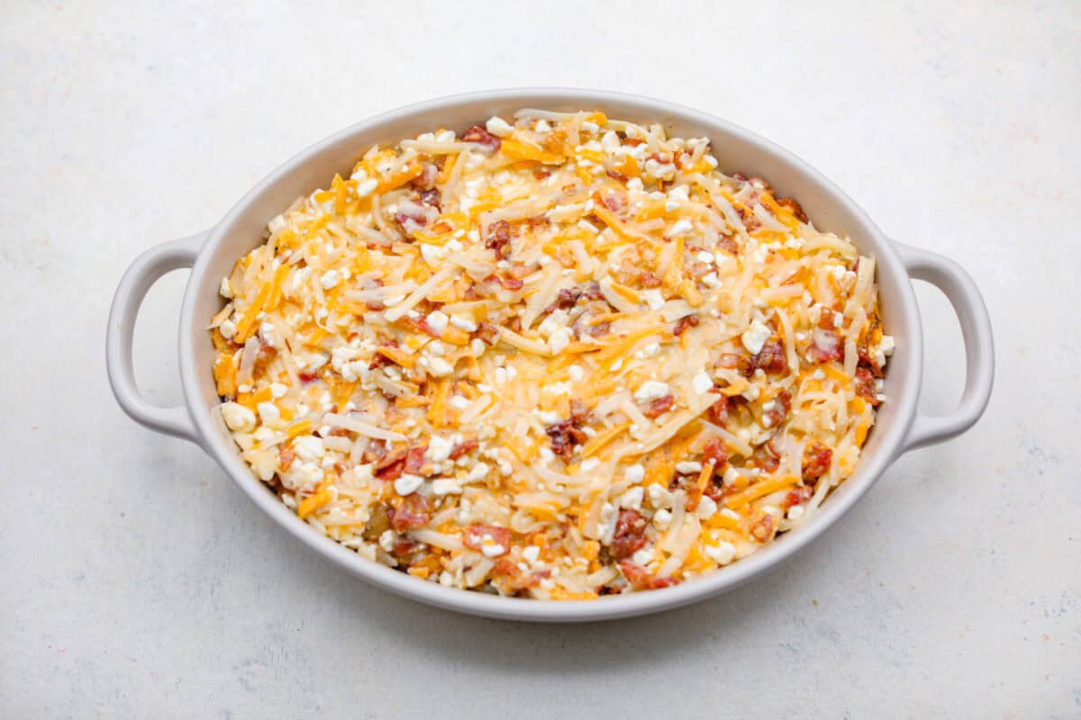 Kickstart your day with this hearty Amish Breakfast Casserole! It's loaded with crispy bacon, tender hash browns, and gooey melted cheese. This dish is a crowd-pleaser that’s perfect for family breakfasts and holiday mornings! Overhead shot of amish breakfast casserole ingredients in a baking dish ready to be cooked.