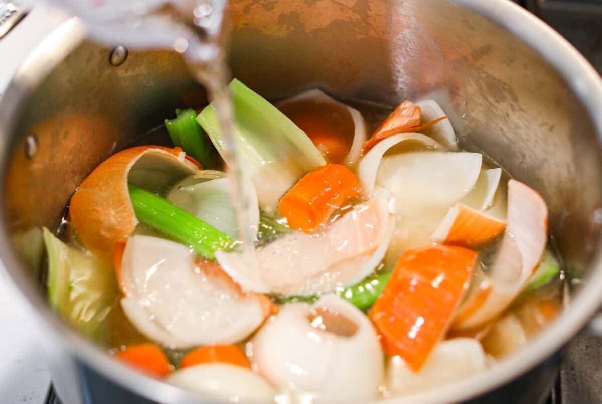 Someone pouring water over the veggies in a pot. 