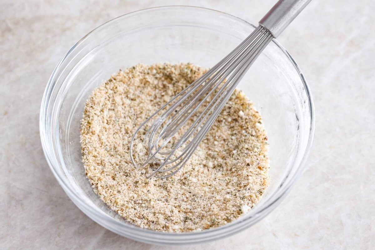 Someone whisking the seasoning and parmesan cheese in a bowl. 