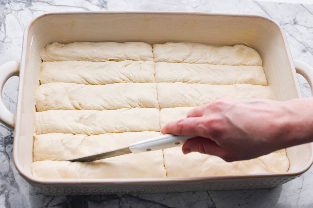 Someone slicing the pizza hut breadsticks dough into 12 even pieces. 