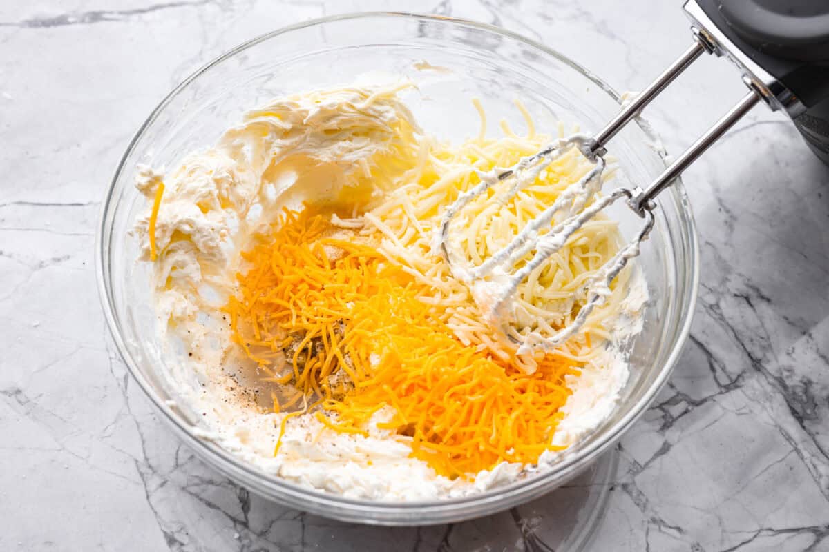 Someone using a hand mixer to make the creamy cheese mixture. 