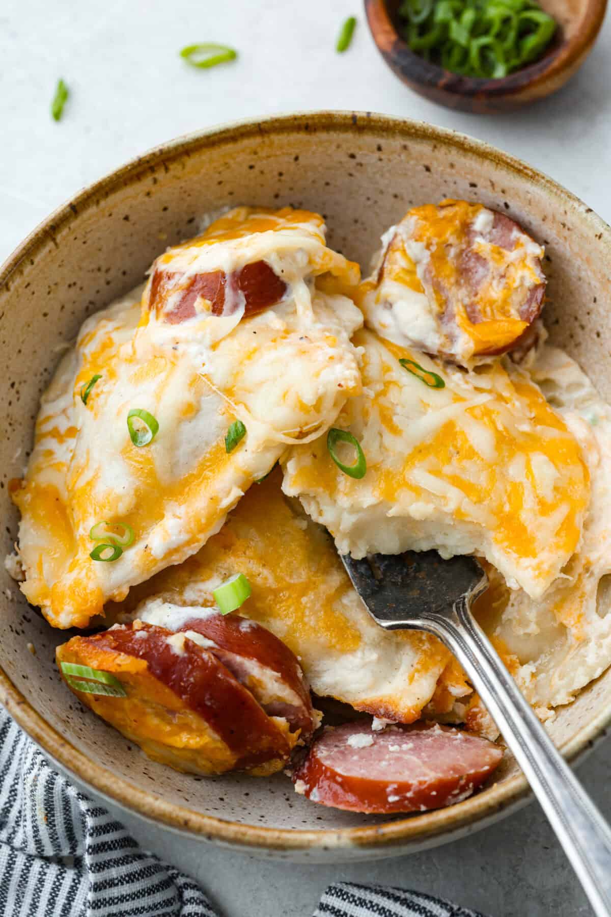 A bowl of pierogi casserole with kielbasa and a fork. 