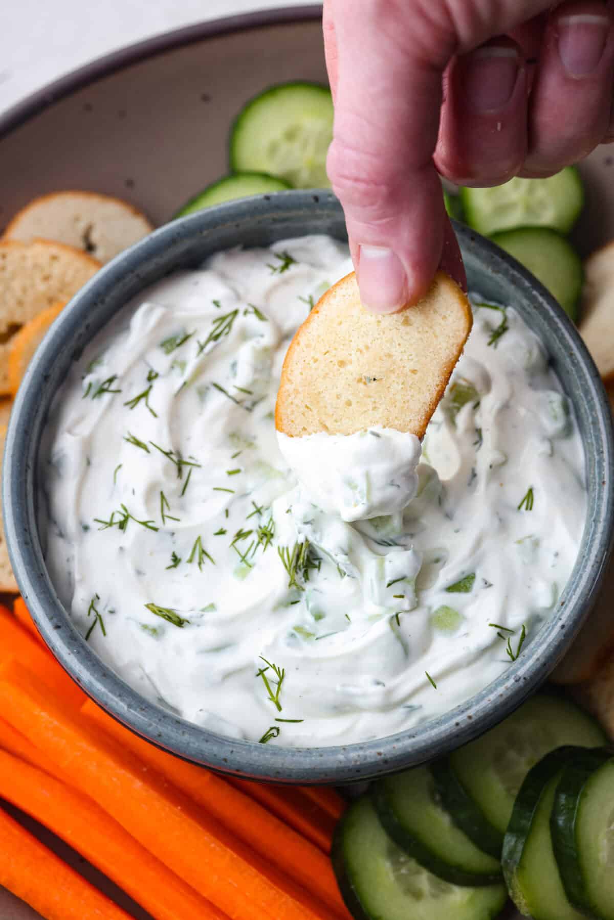 Close up of someone dipping a crostini into the cucumber dip. 