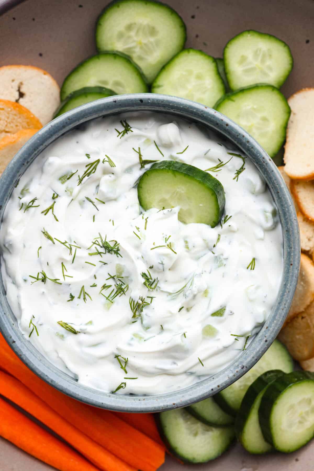 Overhead shot of cucumber dip in a bowl with veggies and crackers on the side. 