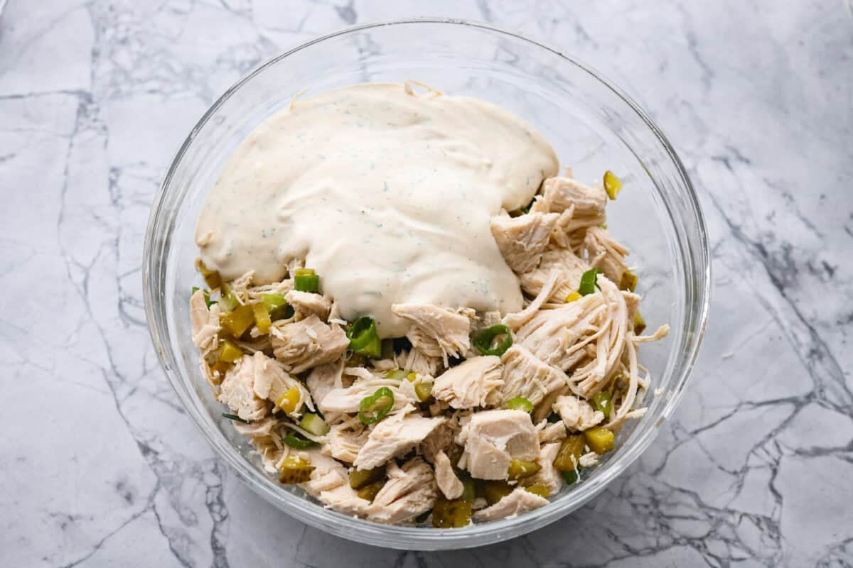 Mixed dressing poured over the chicken mixture in a bowl.