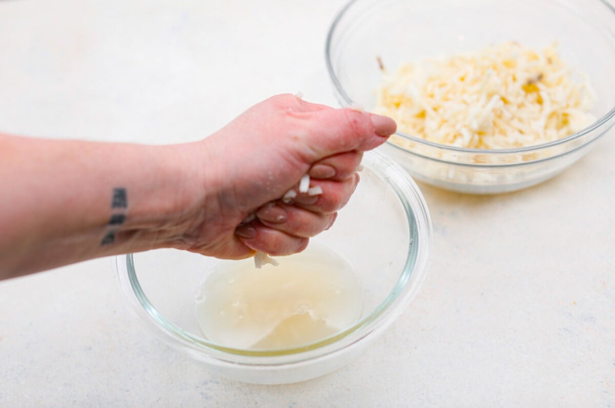 My Hash Brown Crust Quiche is a gluten-free twist on a classic! Crispy, golden potatoes wrap around a rich, savory, custardy filling. Brunch just got an upgrade! Someone squeezing the water out of the hashbrowns.