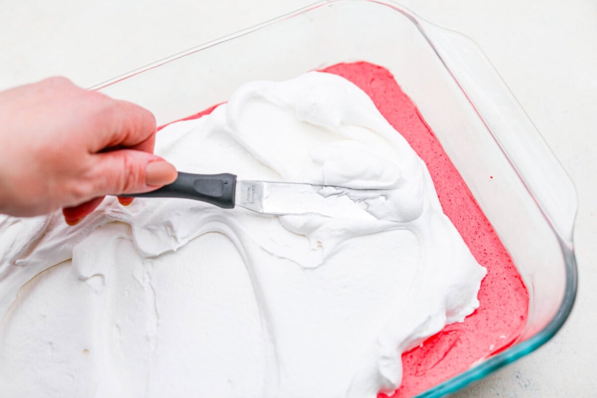 Someone spreading the whipped topping over the jello layer. 