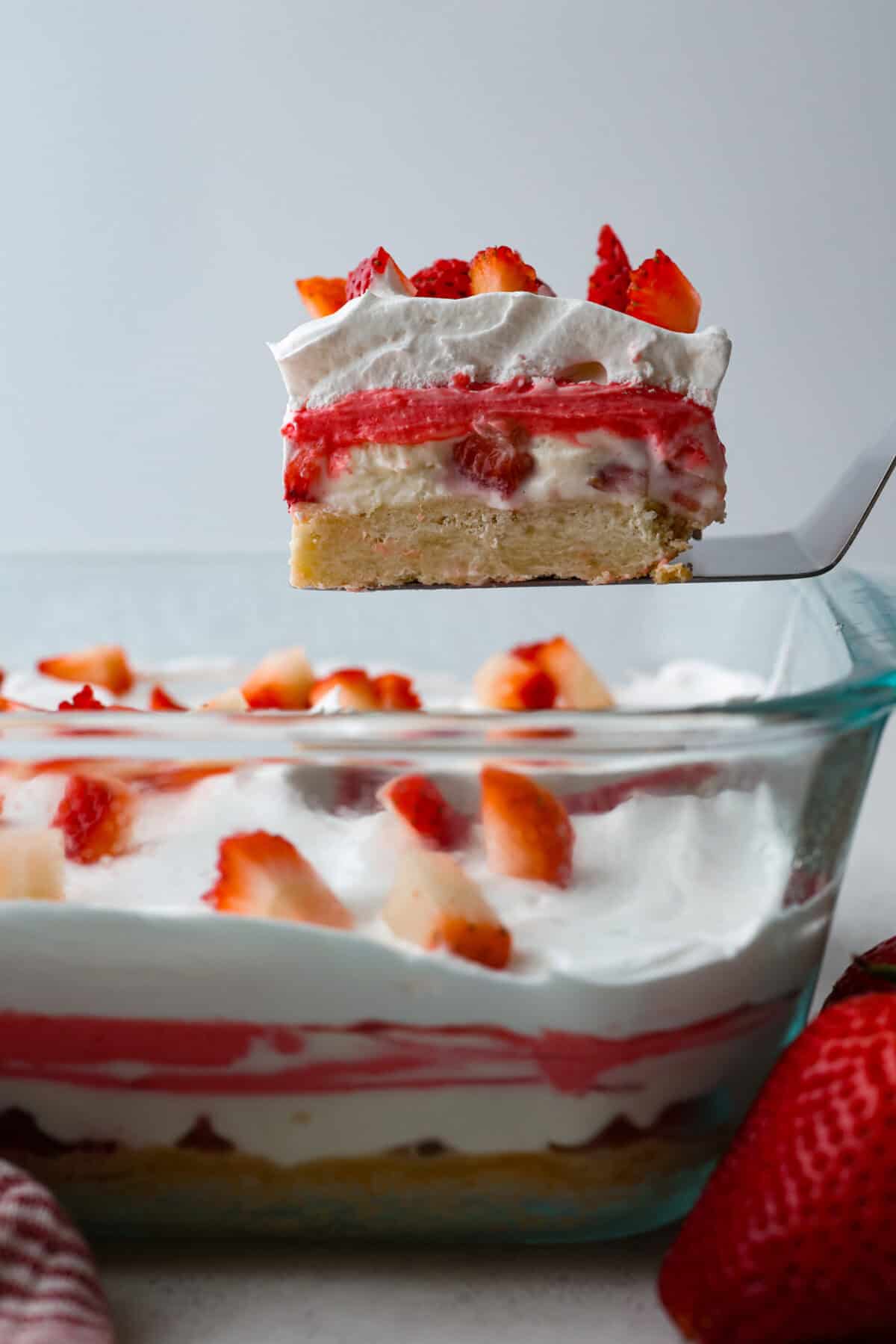 Side shot of someone lifting a slice of strawberry delight our of the baking dish. 
