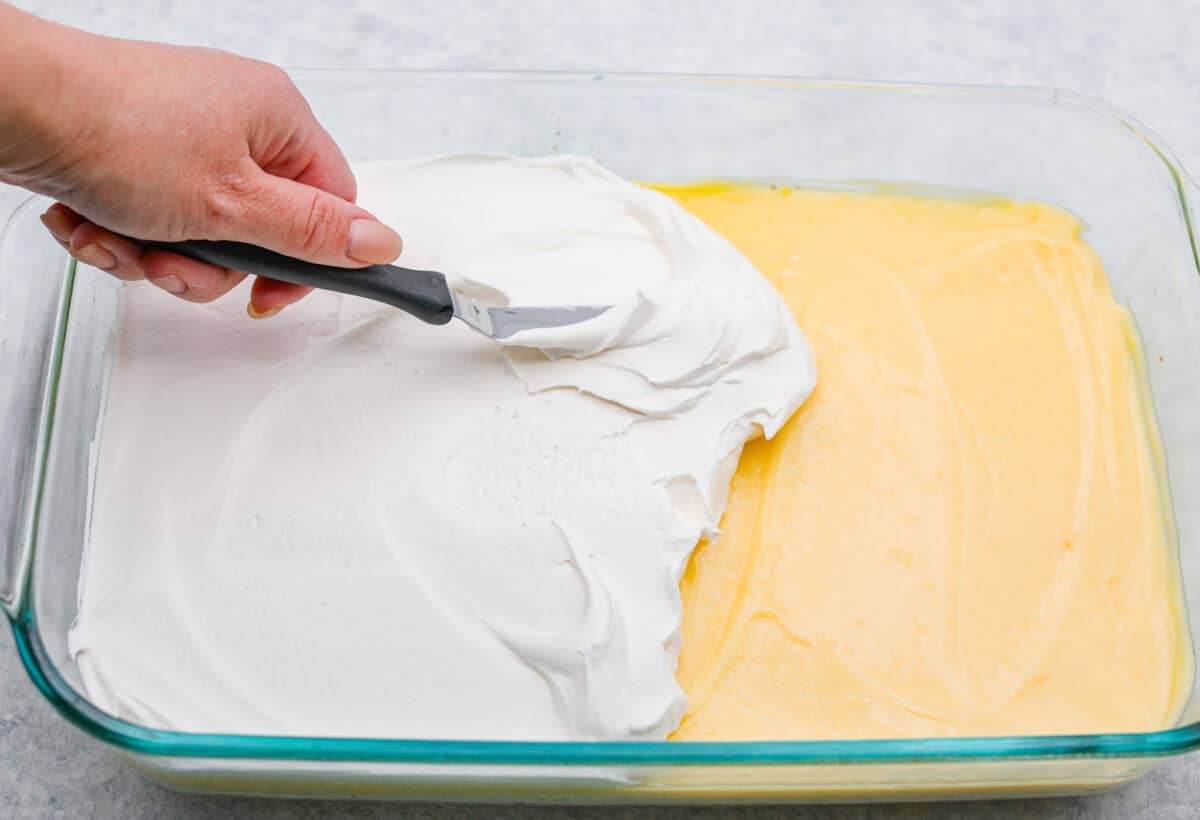 Someone spreading the whipped topping on top of the pudding layer. 
