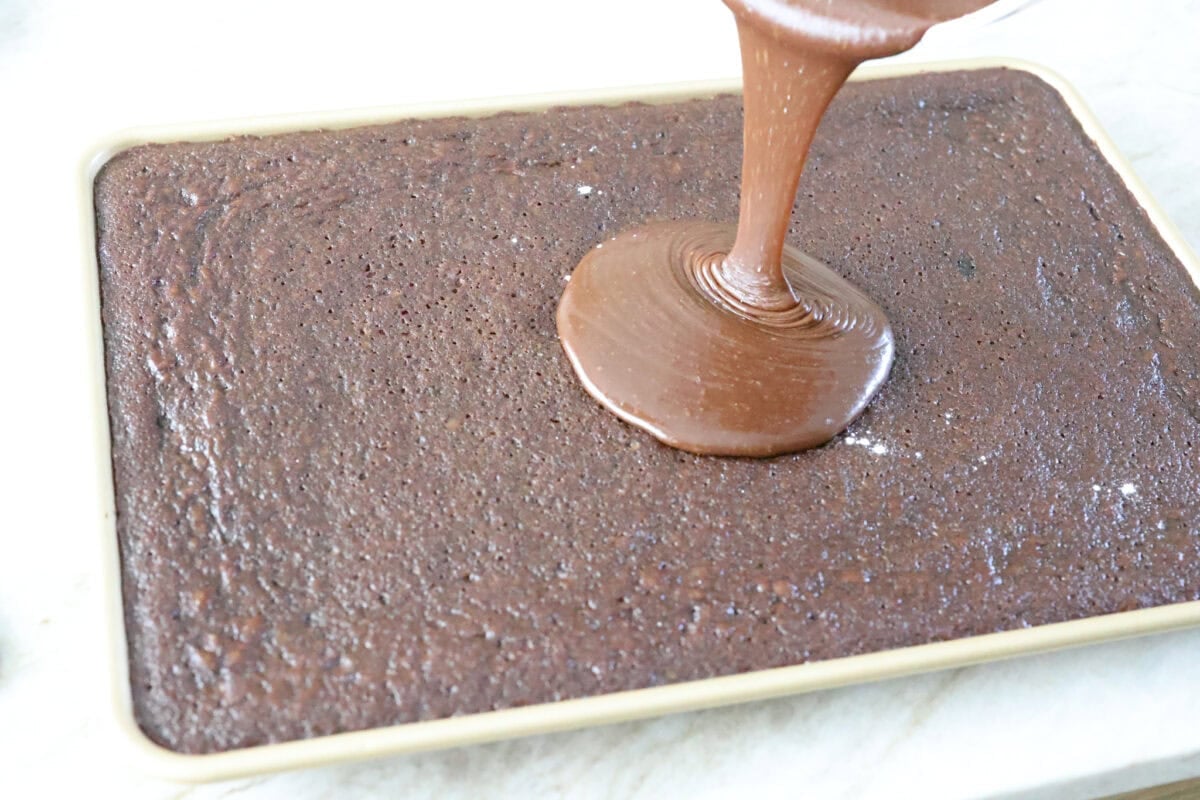 Someone pouring the warm frosting over the warm Dr. Pepper sheet cake. 