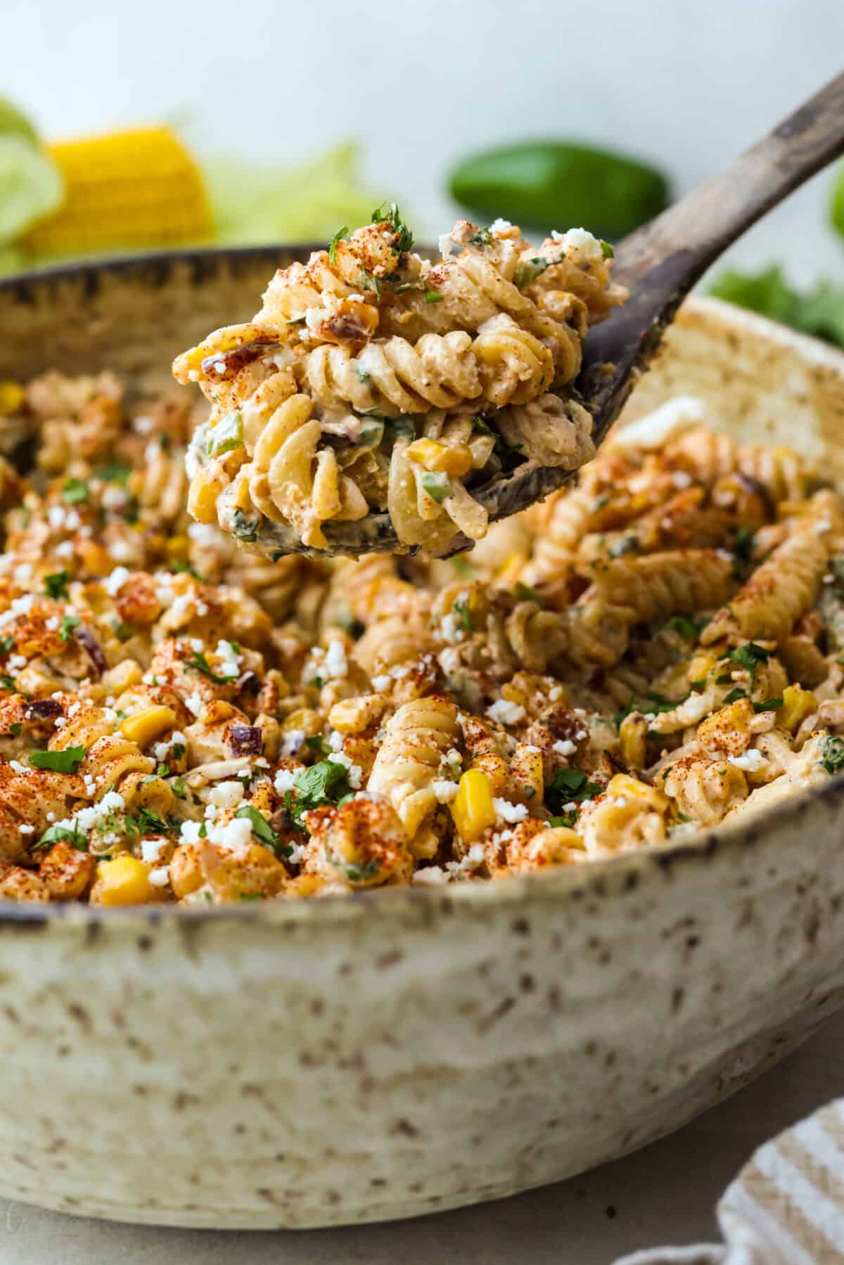 Scoop of elote pasta salad being lifted from a bowl of pasta. 