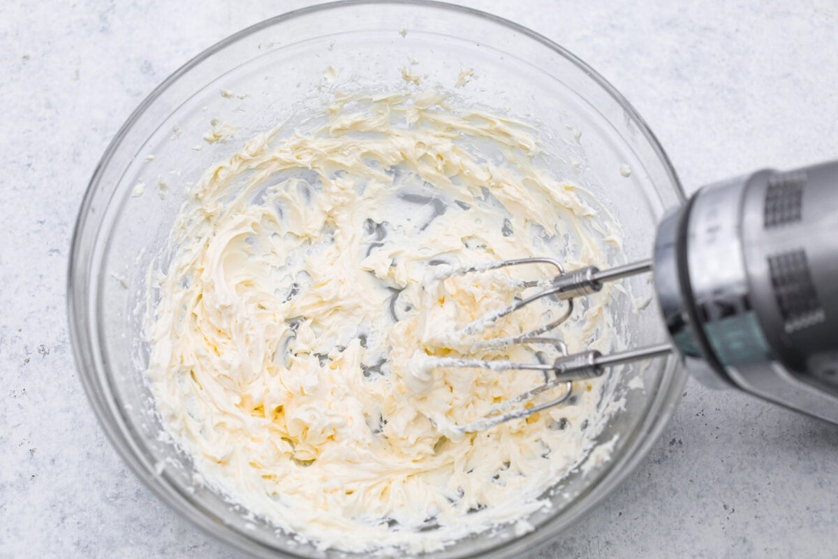 Someone hand mixing cream cheese in a bowl. 