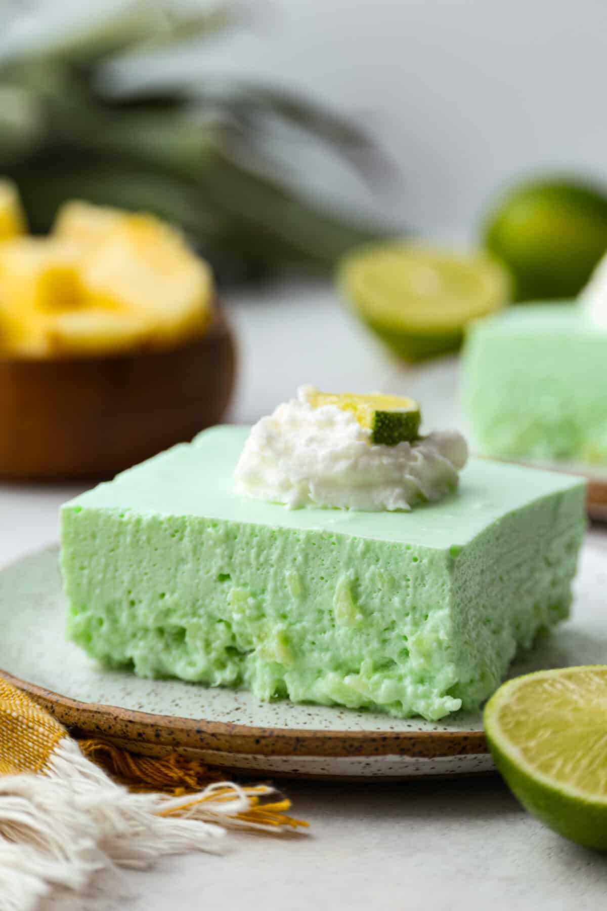 Angle shot of lime Jello salad on a plate topped with whipped cream and a slice of lime. 
