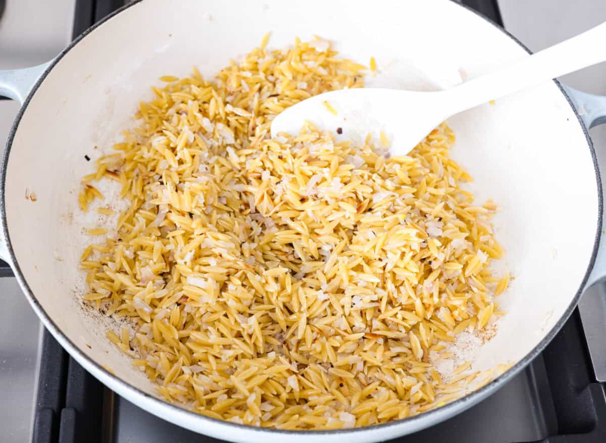Orzo and other ingredients all cooking together in a skillet. 