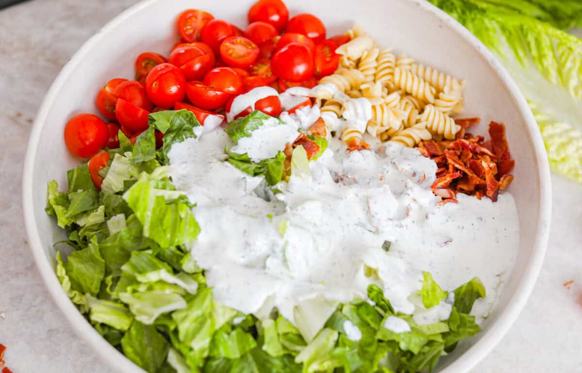 Ranch dressing poured over the pasta, bacon, tomatoes, and lettuce.