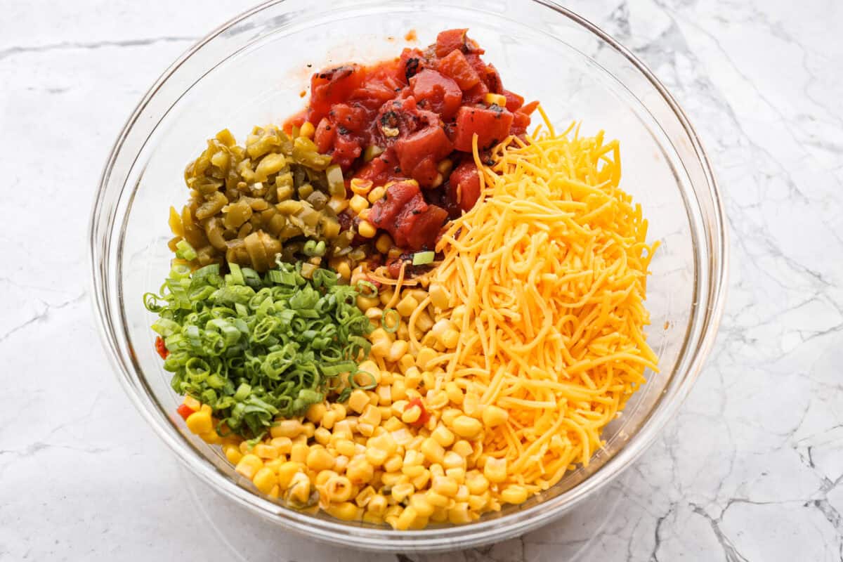 Cheese, jalapeños, tomatoes, corn and green onions, all in a bowl. 