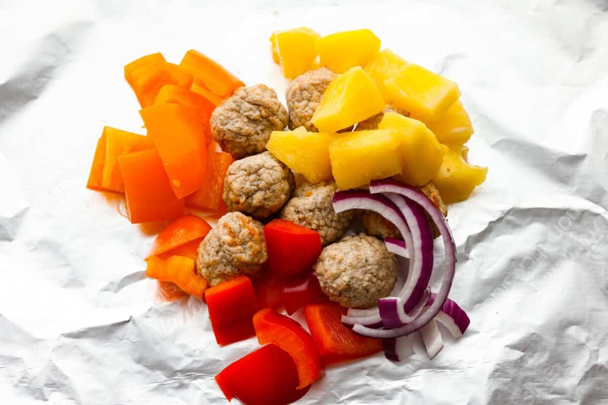 Veggies, pineapple, and meatballs in the middle of the piece of foil. 
