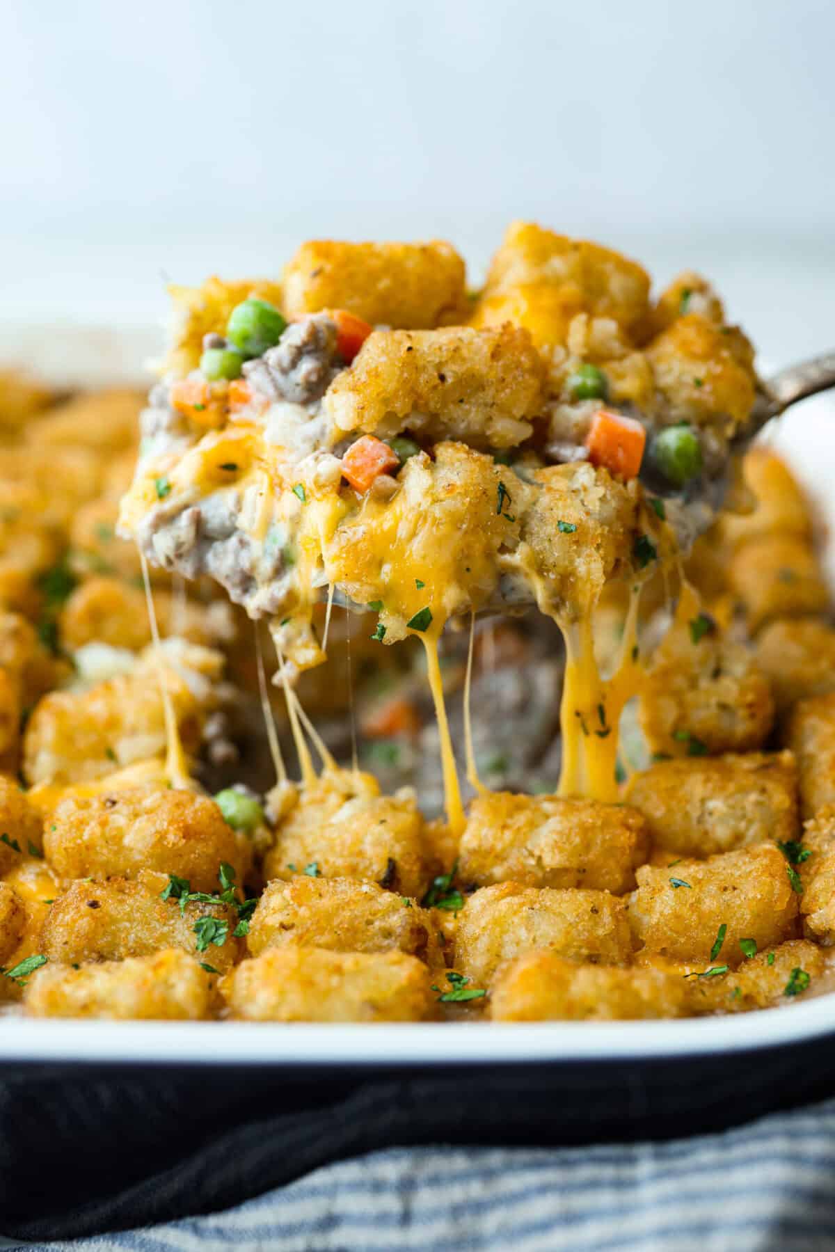 Side shot of a scoop of tater tot casserole being lifted out of the pan. 