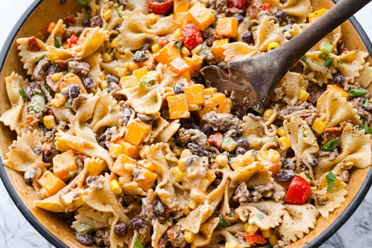 Someone stirring together the pasta salad ingredients with the dressing. 