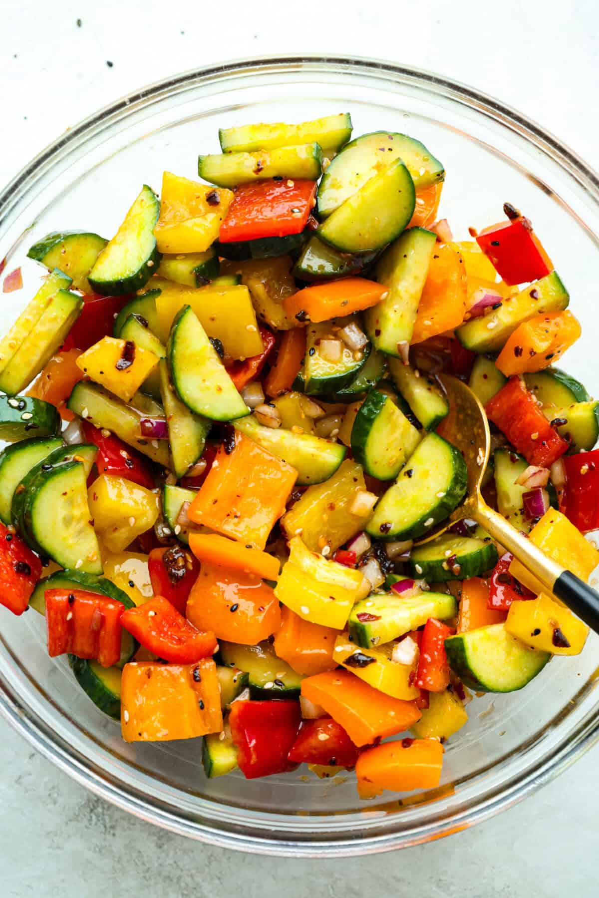 Veggies and dressing mixed together in a bowl to make the cucumber and bell pepper salad. 