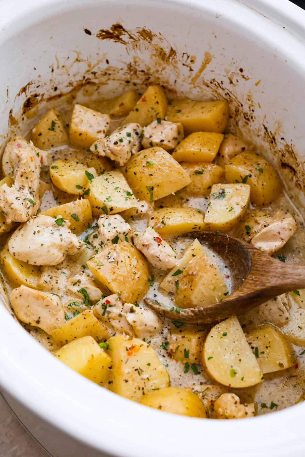 Overhead shot of cooked slow cooker parmesan garlic chicken and potatoes with wood spoon. 