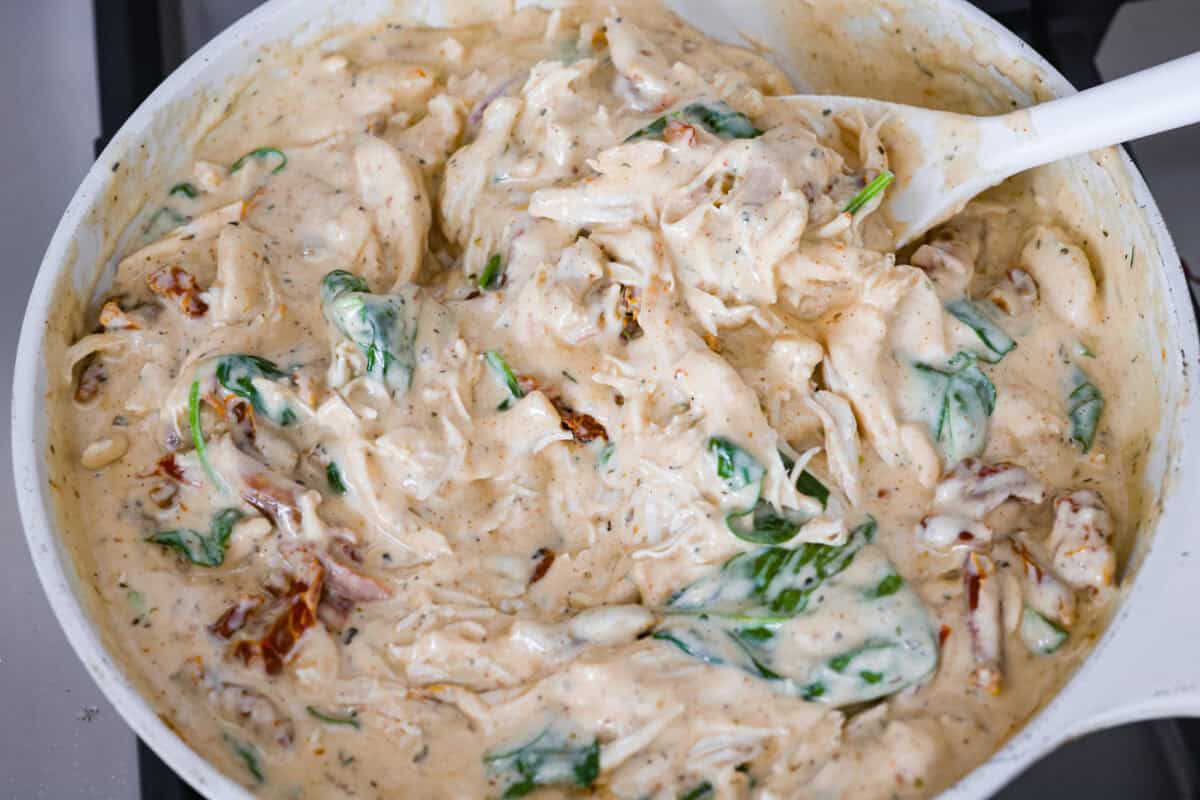 Someone stirring the chicken and spinach into the sauce. 