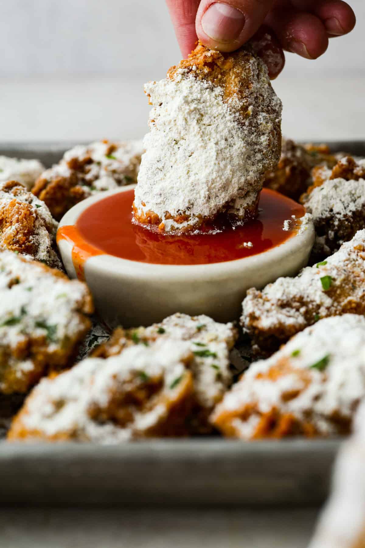 Someone dipping a crack wing into a small bowl of hot sauce.