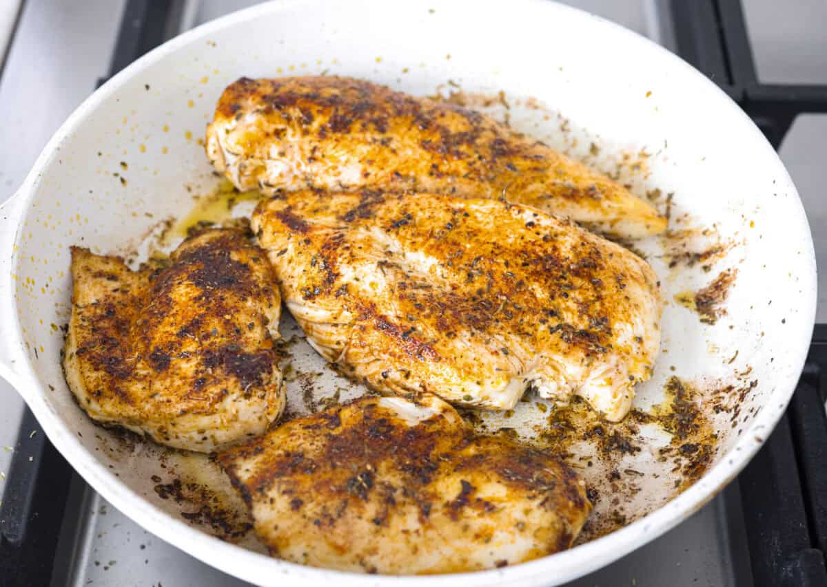 Overhead shot of seasoned chicken cooking in a skillet. 