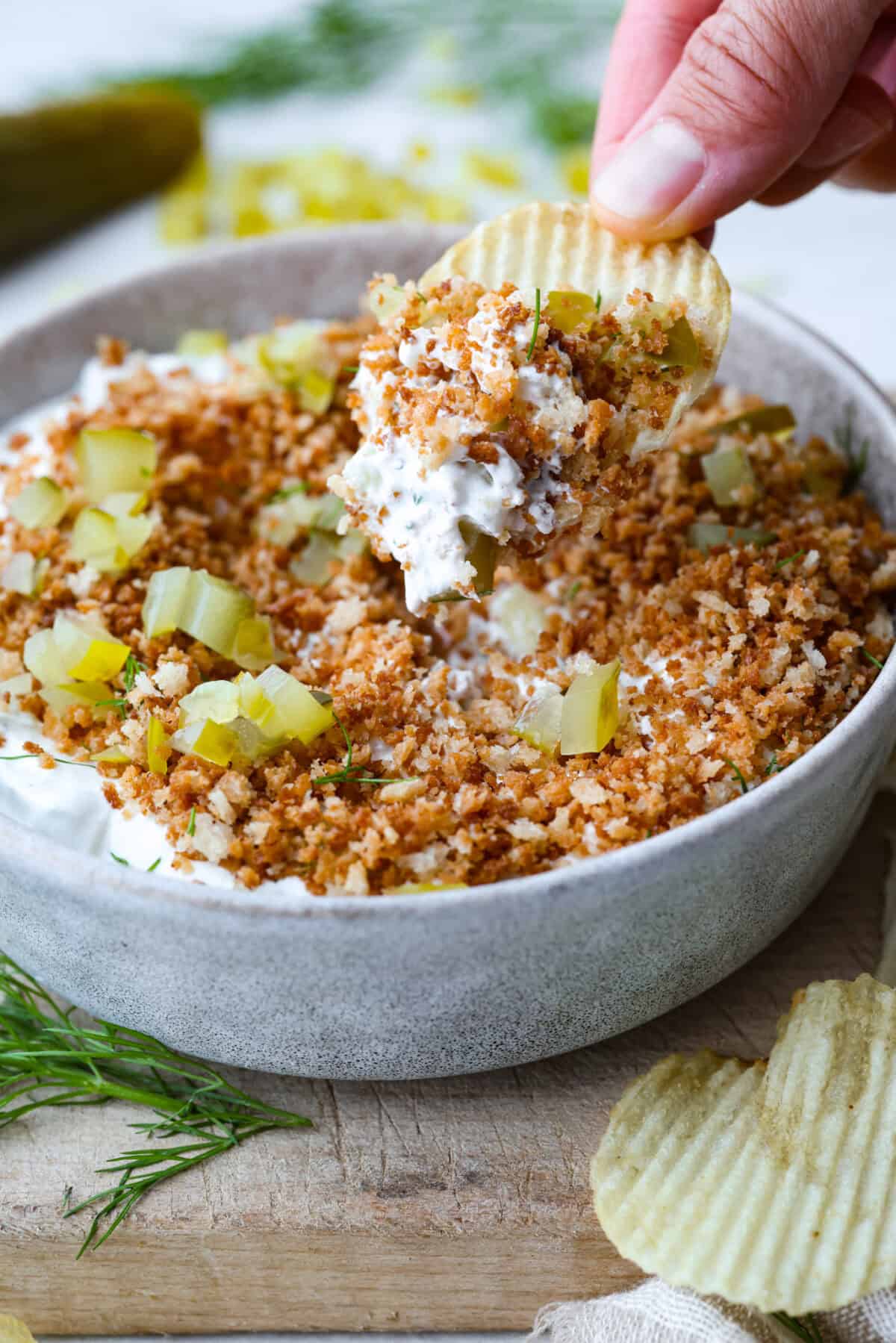 Someone taking a scoop of fried pickle dip with a ruffle chip. 
