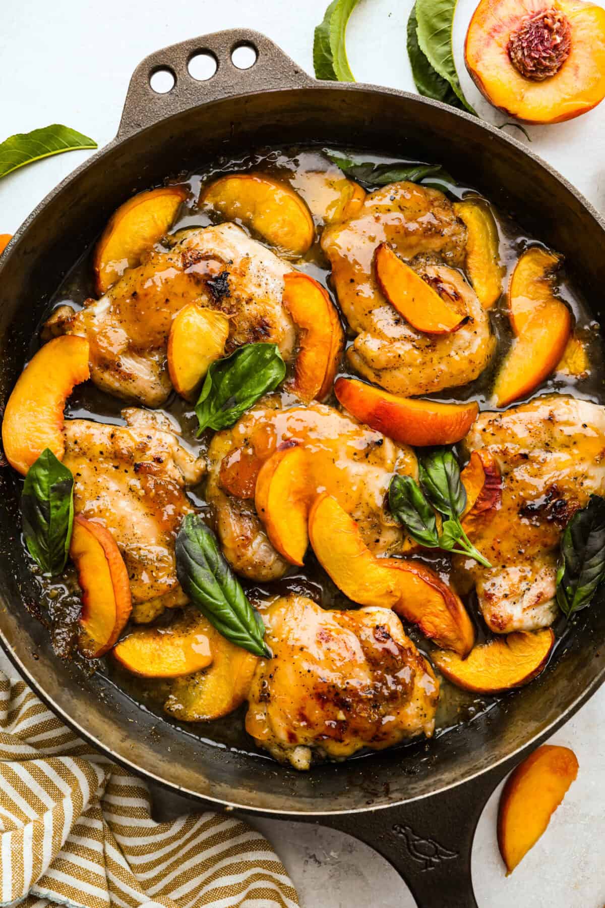 Overhead shot of peach chicken all cooked in a skillet garnished with fresh basil leaves. 