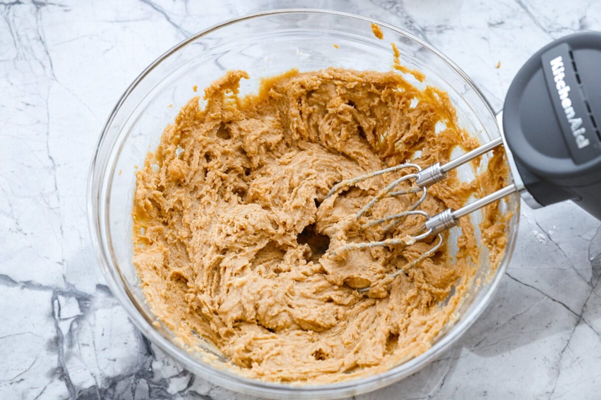 If you grew up in Utah, Lunch Lady Peanut Butter Bars were basically a rite of passage. Thick, chewy, and slathered in chocolate frosting. My version is even better, and yes, this one earned its spot in my cookbook for a reason. Someone mixing butter, brown sugar, and peanut butter in a bowl with a hand mixer.