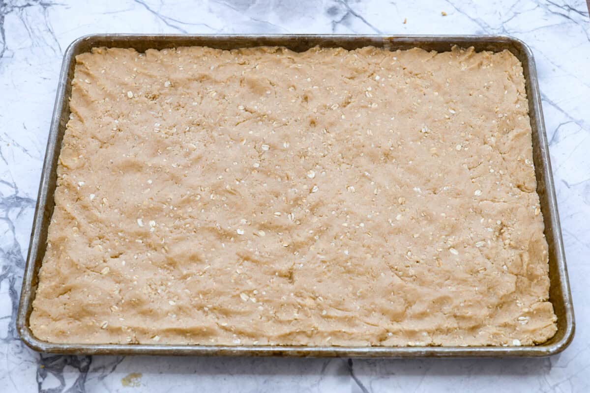 If you grew up in Utah, Lunch Lady Peanut Butter Bars were basically a rite of passage. Thick, chewy, and slathered in chocolate frosting. My version is even better, and yes, this one earned its spot in my cookbook for a reason. Bar batter smashed and spread out into a cookie sheet.