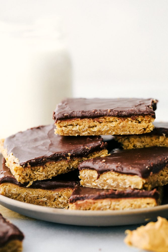 These peanut butter bars are thick, rich, and heavenly! A thick layer of peanut butter mixed with rolled oats makes a creamy filling with a smooth chocolatey frosting that is an irresistible combination. A stack of peanut butter bars on a gray plate/