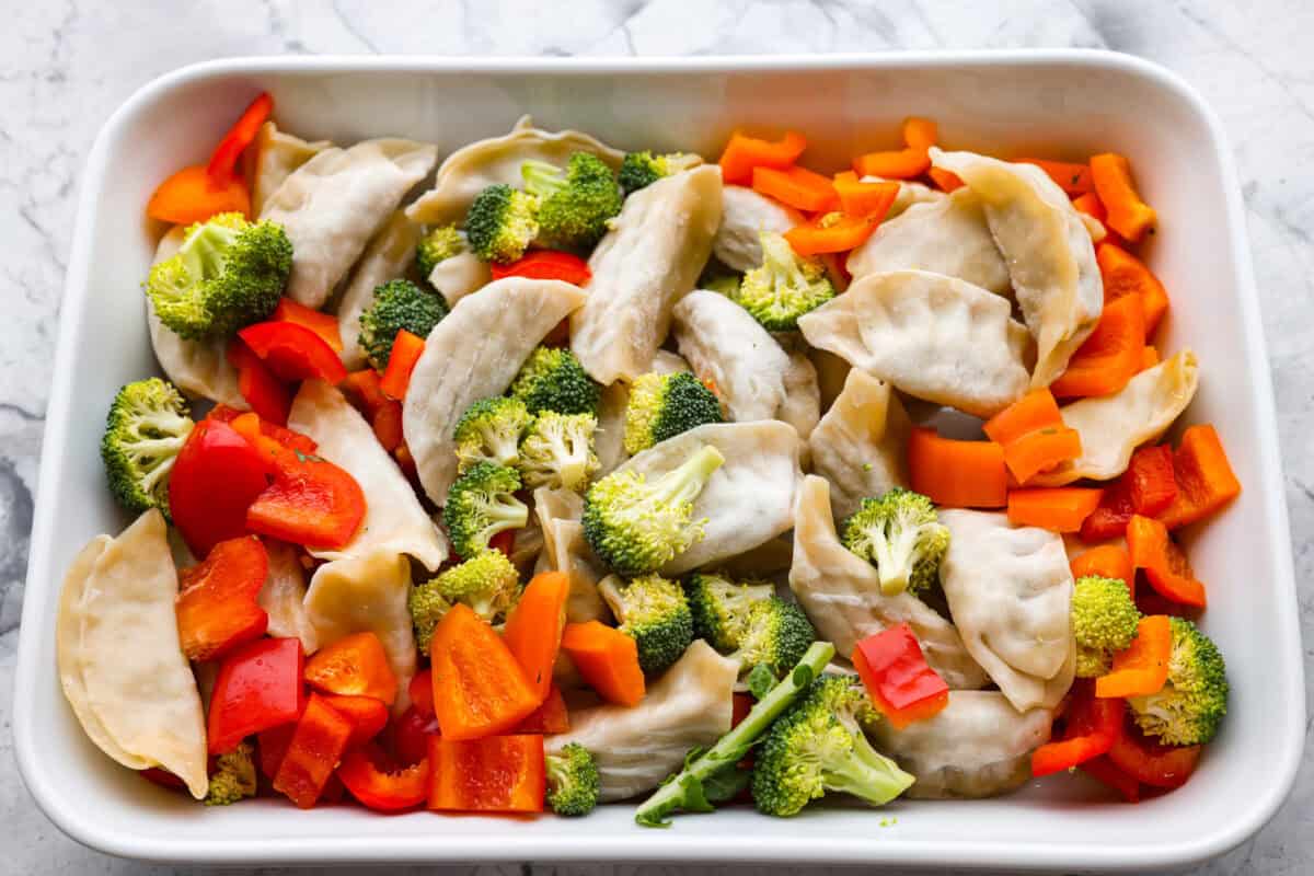 Potstickers added to the bottom of a casserole dish with vegetables added to the top. 