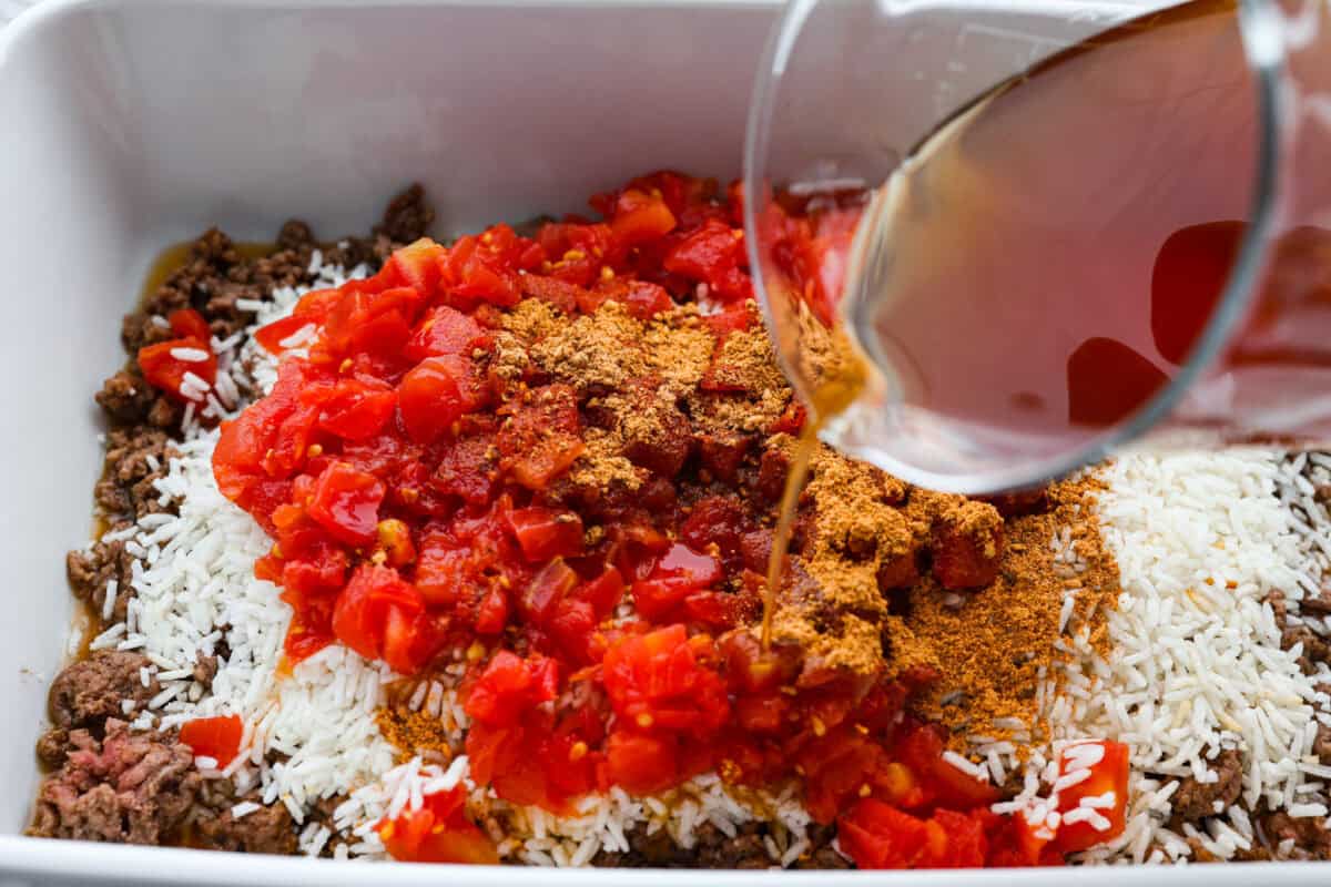 Someone pouring beef broth into the rice and beef mixture. 