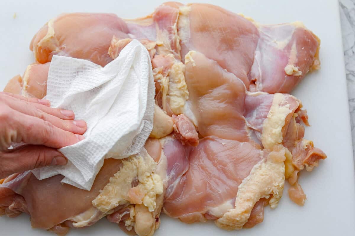 Someone dabbing the chicken thighs dry with a paper towel. 