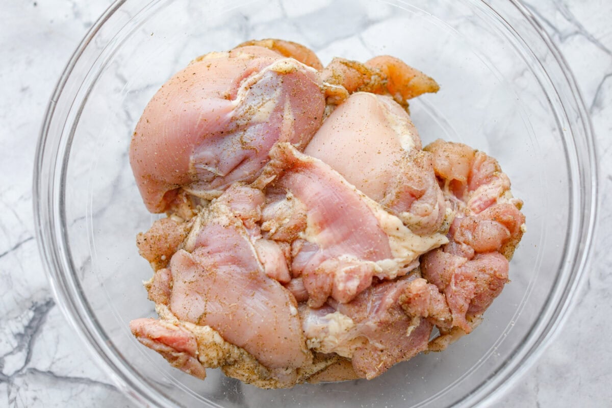 Chicken thighs coated with seasonings sitting in bowl.