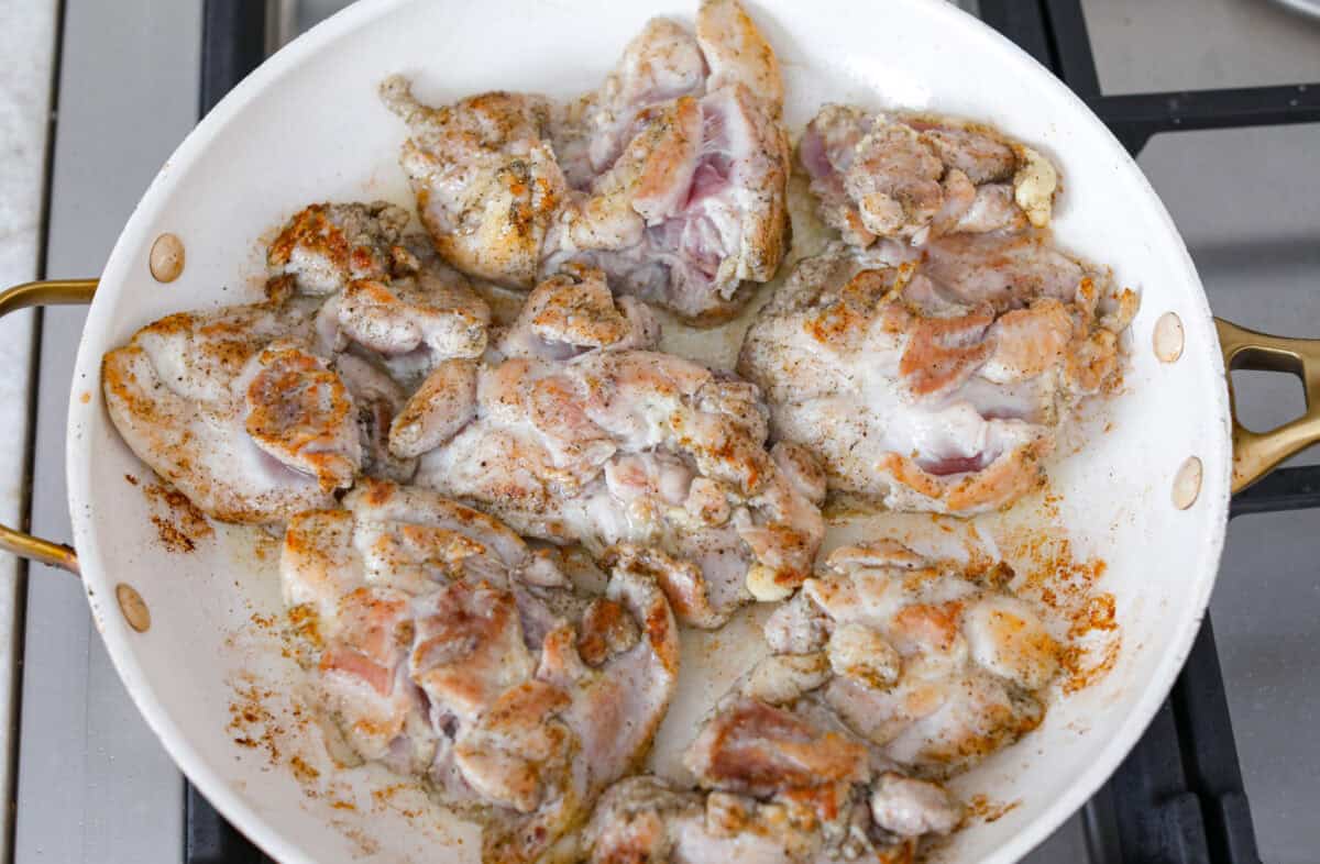 Chicken thighs browned and cooking in a skillet.