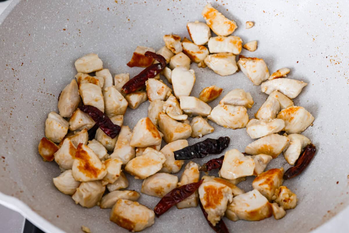 Dried peppers added to the chicken cooking in a skillet.