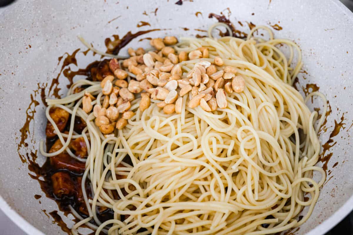 Cooked noodles and peanuts added to the sauce and chicken in the skillet.