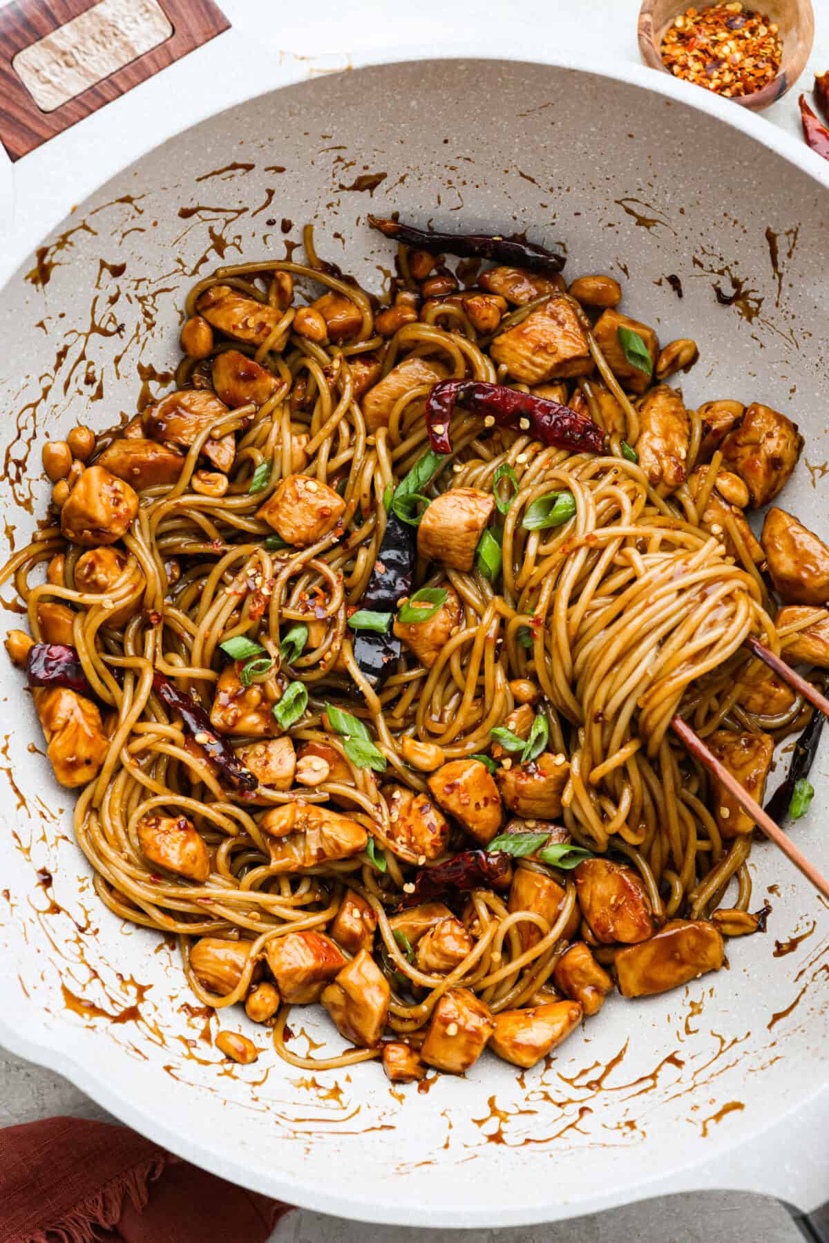 Overhead shot of someone tossing the sauce in with the Kung Pao chicken noodles.