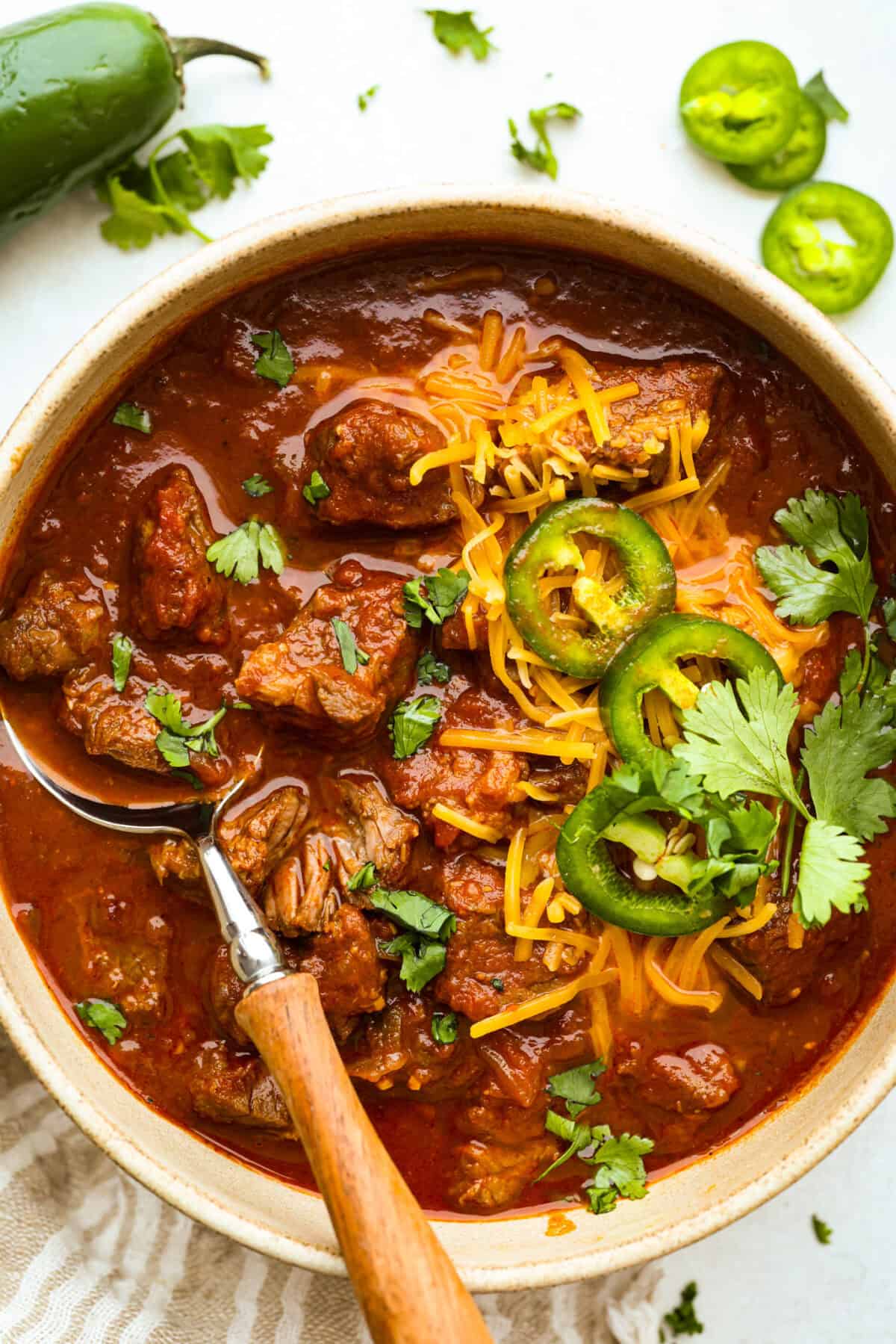 Do you like your chili with beans or without? This authentic Texas chili keeps it classic. Just bold, tender chuck roast, without beans. It has a rich, smoky flavor in every bite. Bowl of Texas chili garnished with shredded cheese, jalapeno slices, and fresh cilantro.